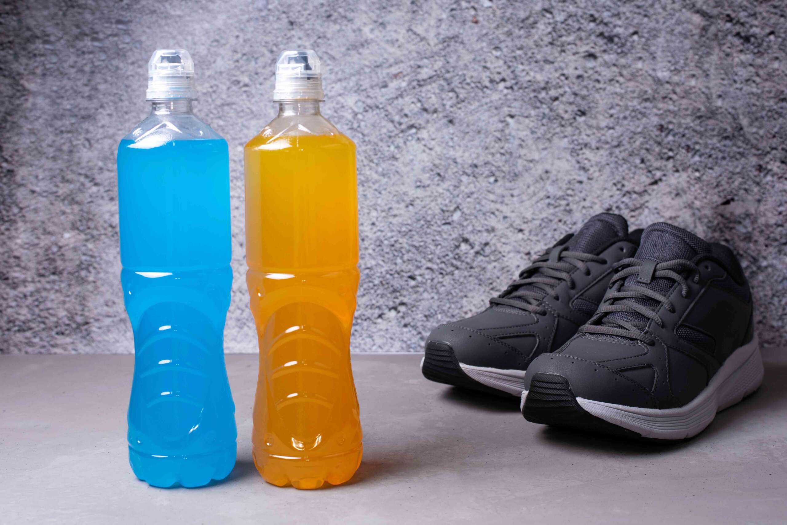 Two bottles of isotonic drink, restoring water and salt balance after exercise on a gray background, a healthy drink after sport activity, close up.