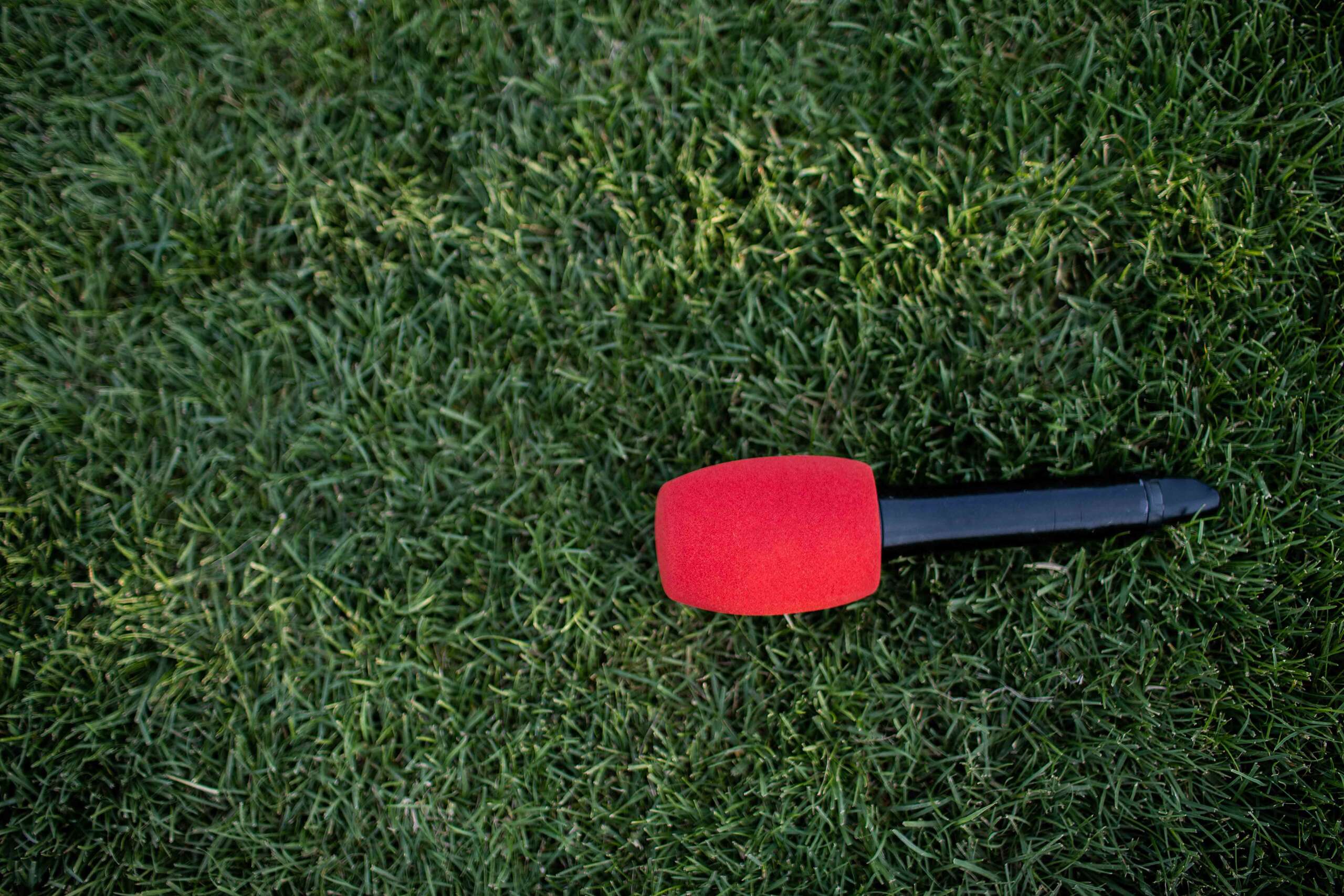 Black - red handheld wireless Mic laid down on the green grass for all type of event activities. microphone for announcing outdoor sport and announcement concept design with copy space.